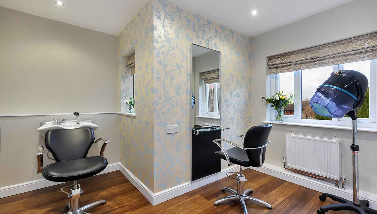 A modern hair salon with two black styling chairs in front of a large mirror and a window providing natural light.