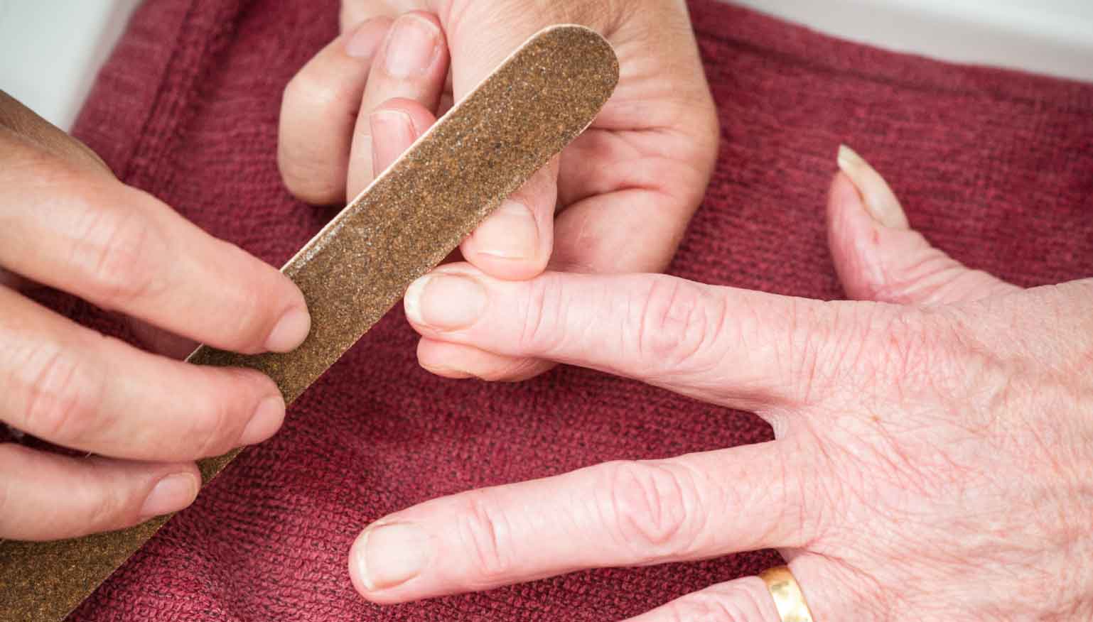 Close-up of a person filing another person’s fingernails with a brown nail file.