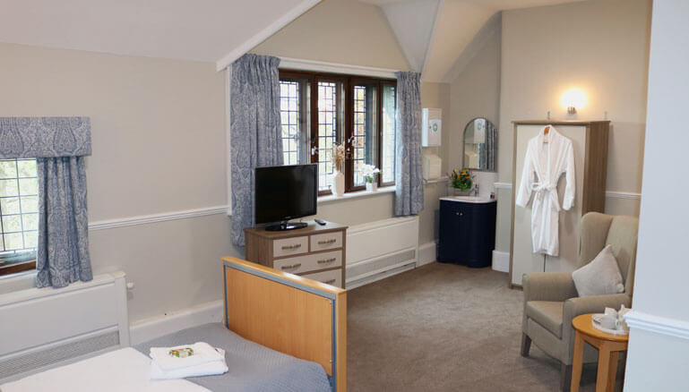 Elegantly furnished bedroom with two armchairs, a  TV, and a window with curtains.