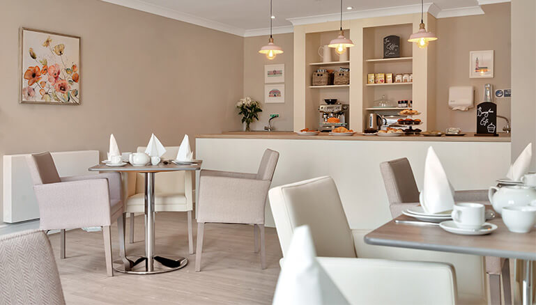 A modern cafe interior with neatly arranged tables and chairs, white tablecloths, pendant lights, and a serving counter in the background