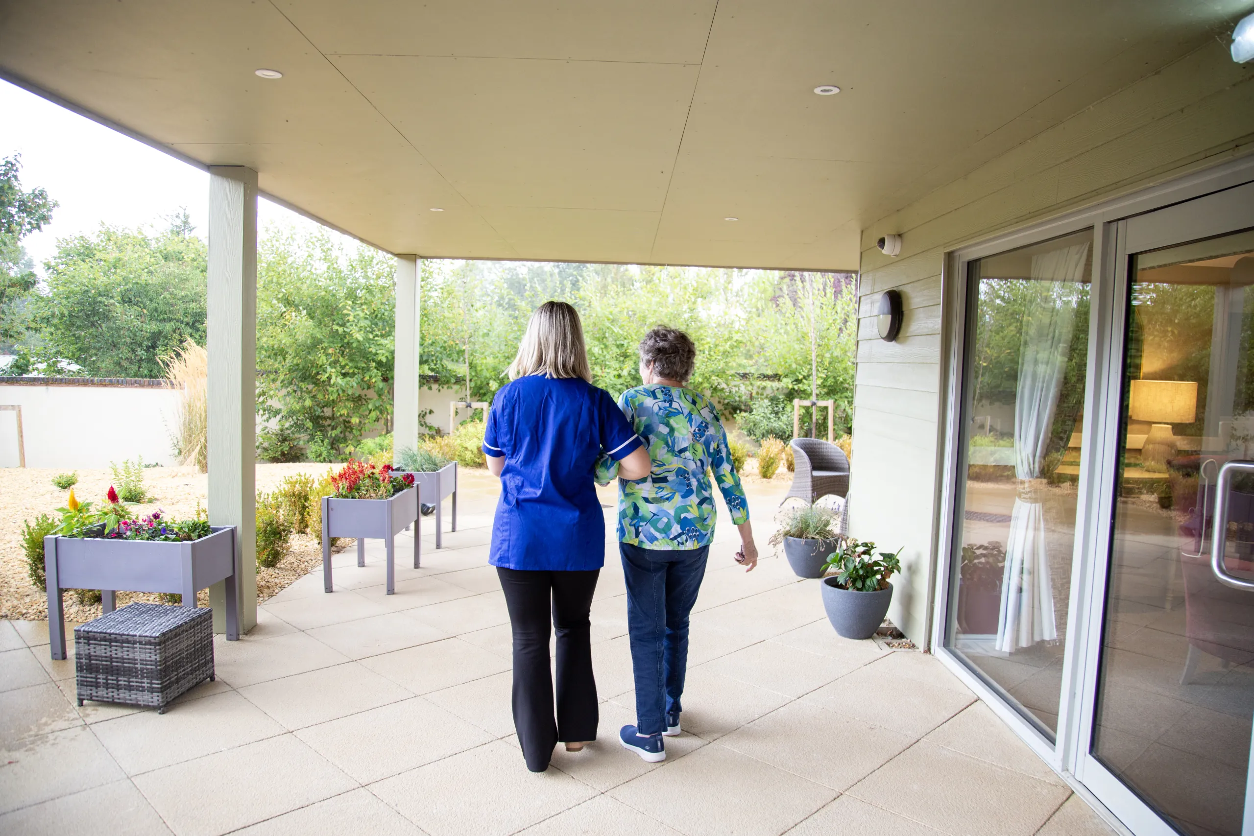 A member of the Colwall care team walking arm in arm with a resident along the home's planted garden terrace