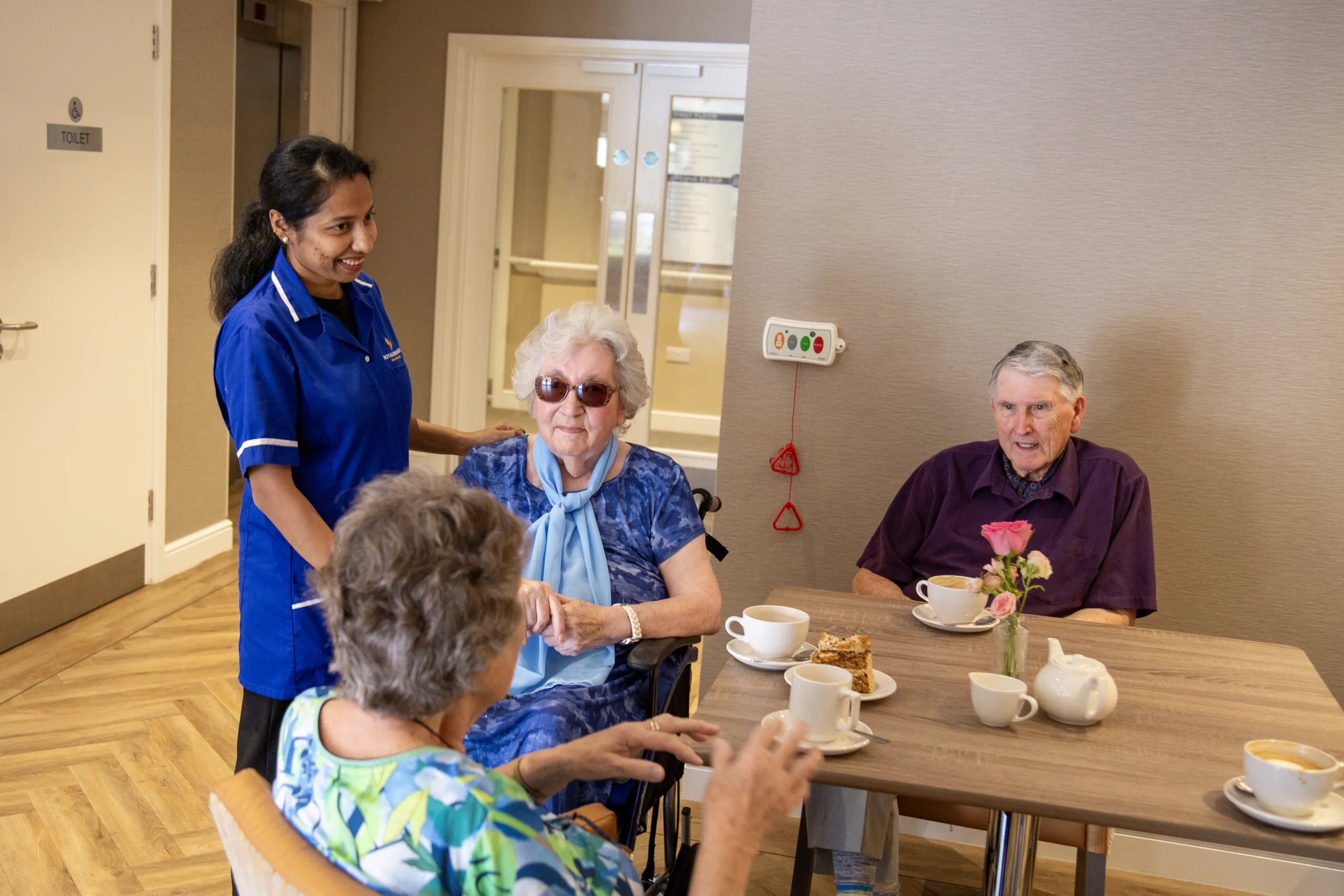 A nurse chatting with three residents around a table over afternoon tea at Colwall Care Home