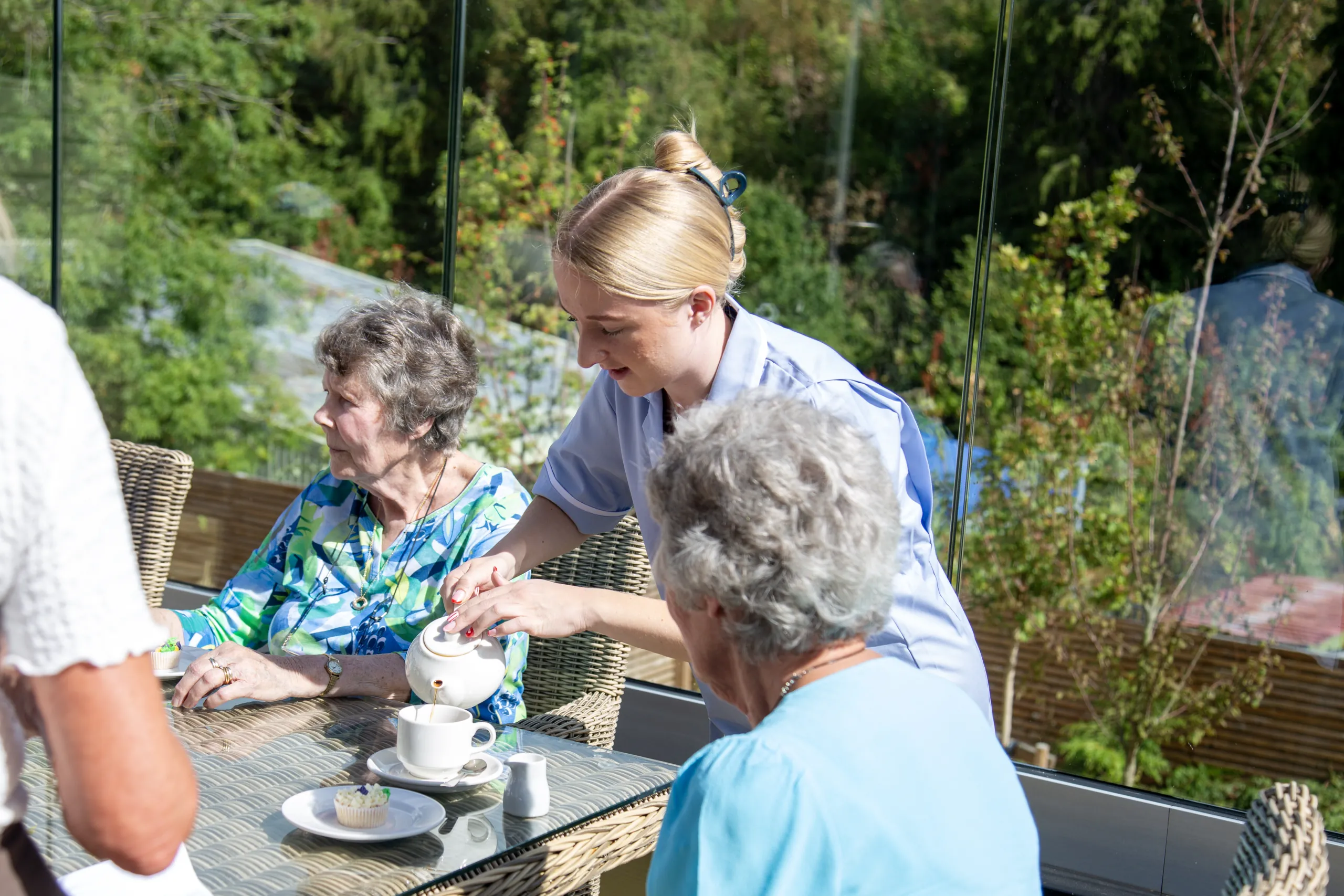 A carer serving tea to residents seated on the terrace at Colwall Care Home