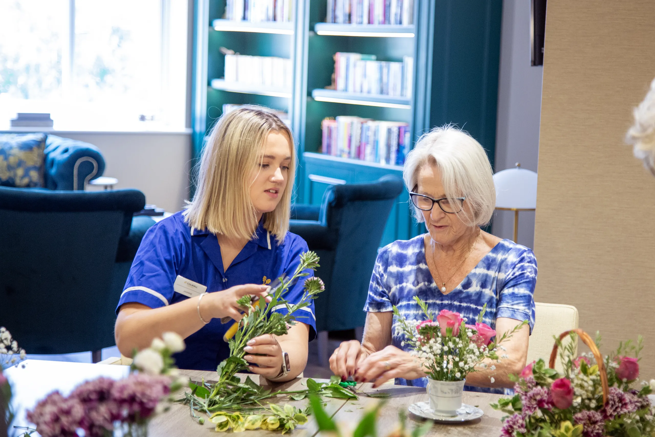 A resident flower arranging alongside a member of the Colwall team in the library area