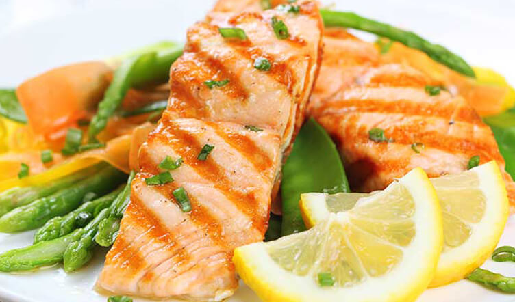 A plate of grilled salmon with asparagus, carrots, and lemon slices garnished with chopped herbs