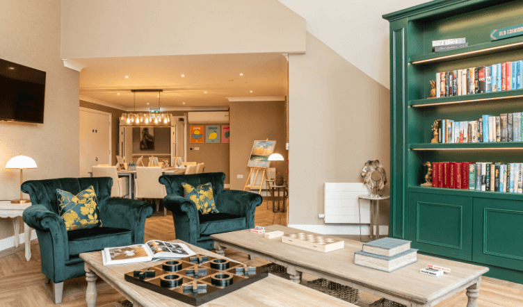 Two emerald velvet chairs behind two low coffee tables and a large green bookcase