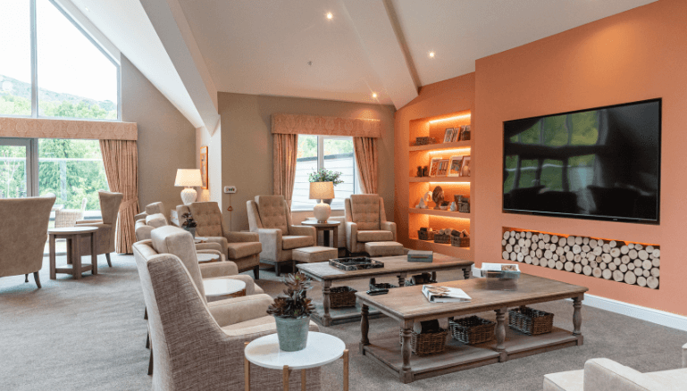 Large room with television set into the wall, decoration shelves and various seats around a low rise coffee table