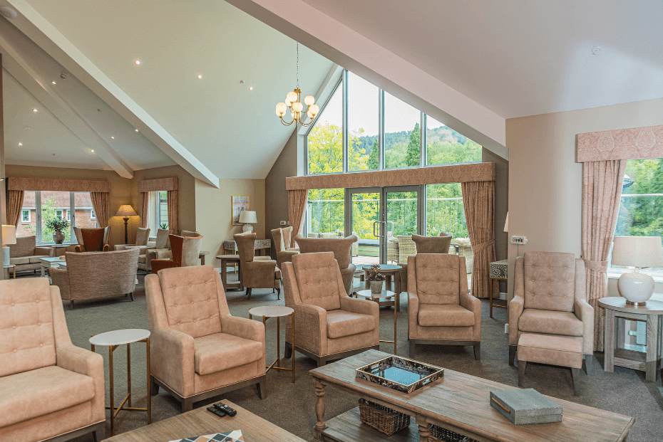A large apex window with chandelier and various beige armchairs and coffee tables 