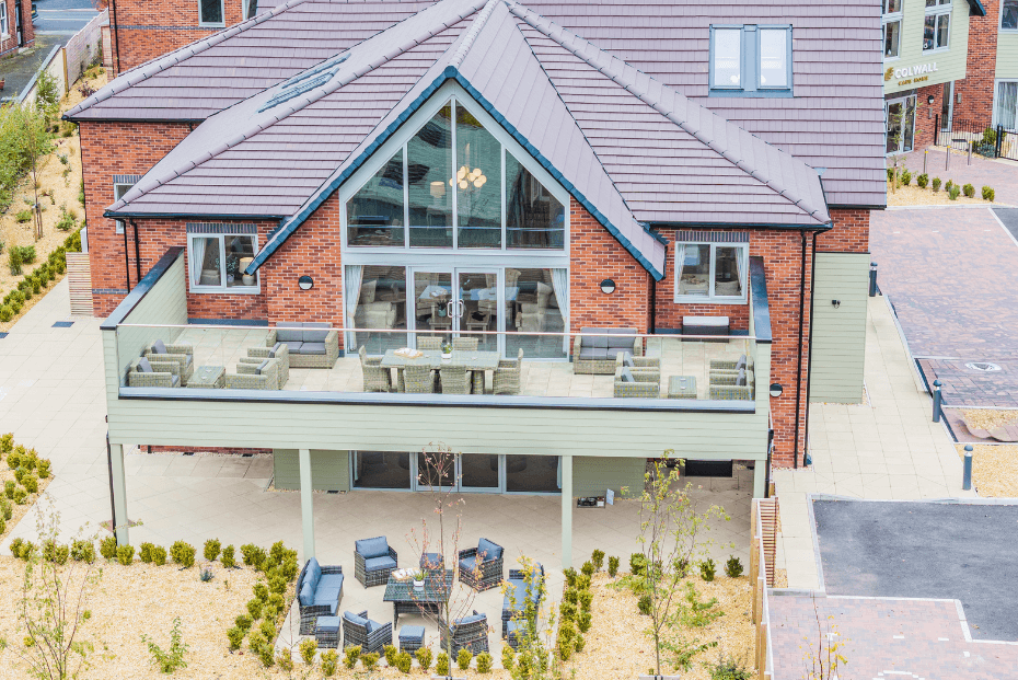 A redbrick building with a first-floor terrace balcony arranged with outdoor furniture