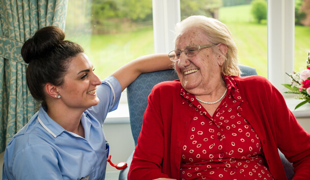 A healthcare worker and an elderly lady smile at each other