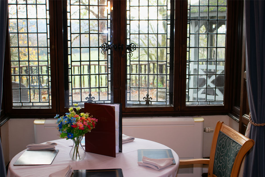 Dining setup for two with a vibrant bouquet, near large windows overlooking a serene view of outside gardens