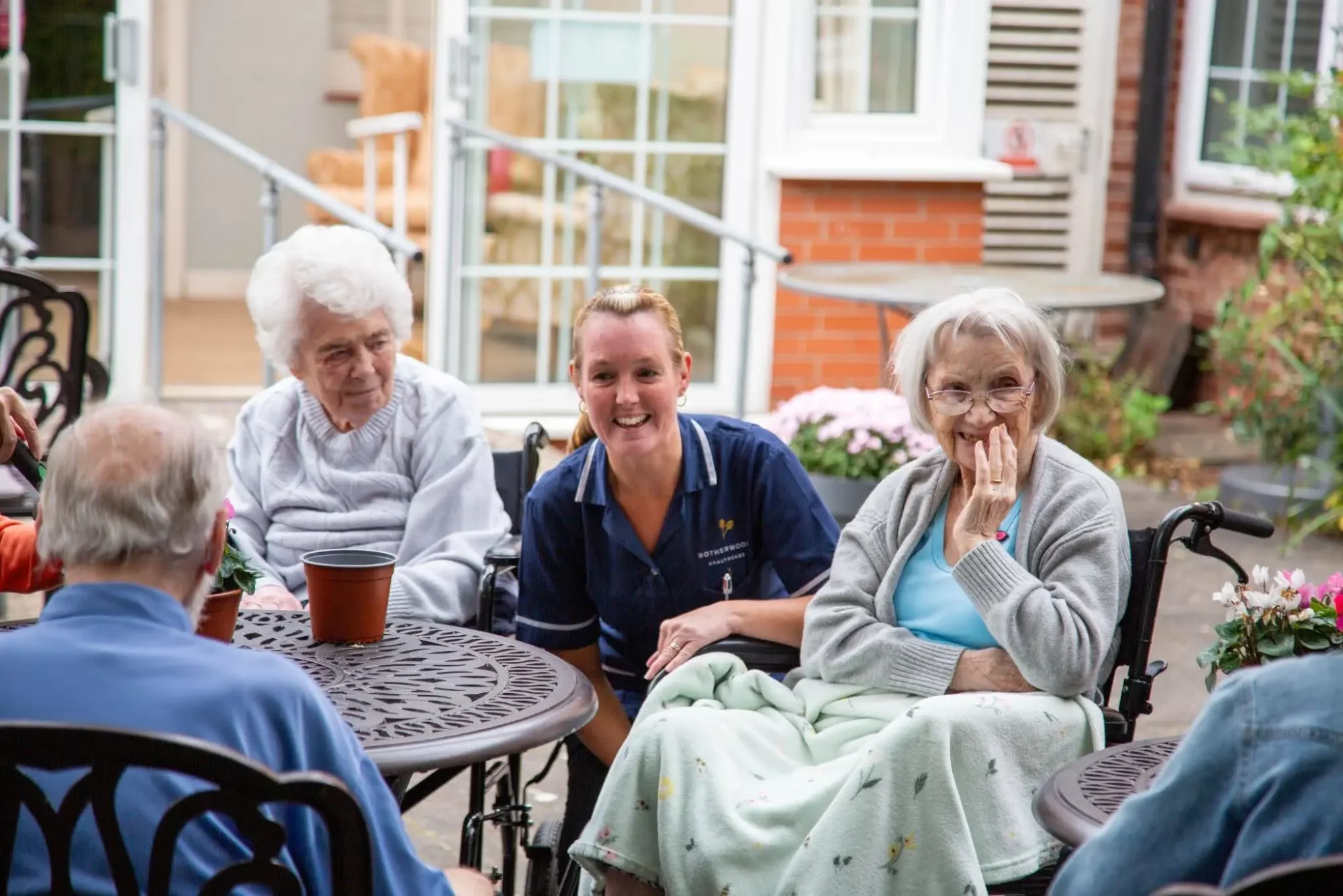A nurse laughing with residents seated around a table on the garden terrace at Dorset House