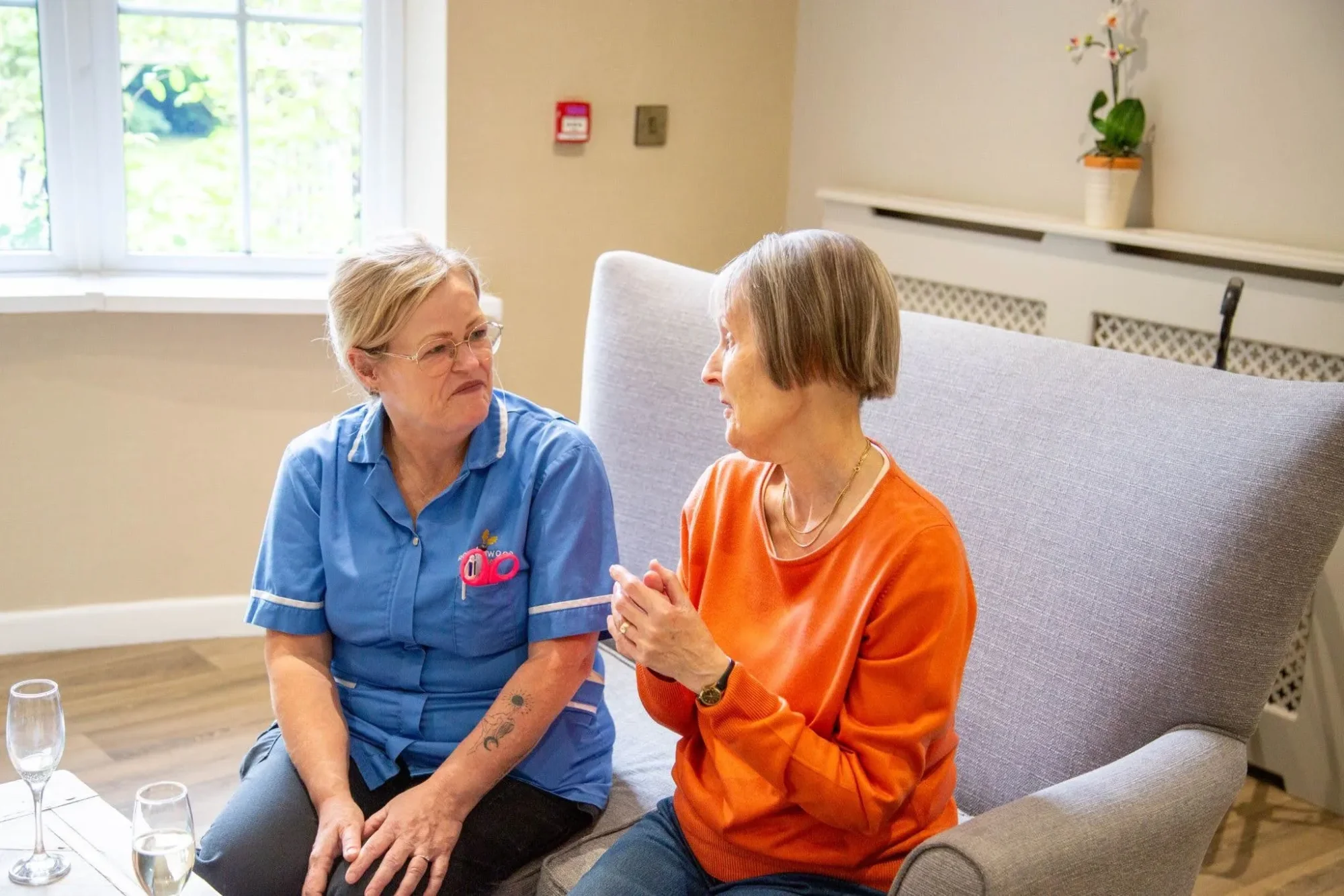 A nurse sitting on a sofa in conversation with a resident in the Dorset House lounge