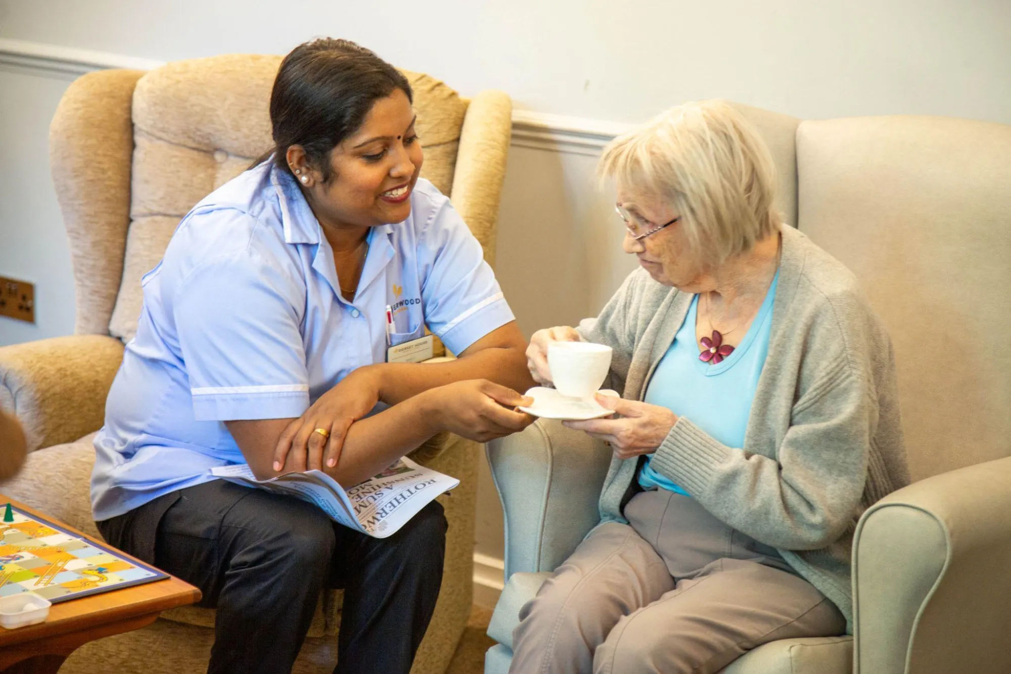 A nurse handing a cup of tea to a resident seated in an armchair at Dorset House