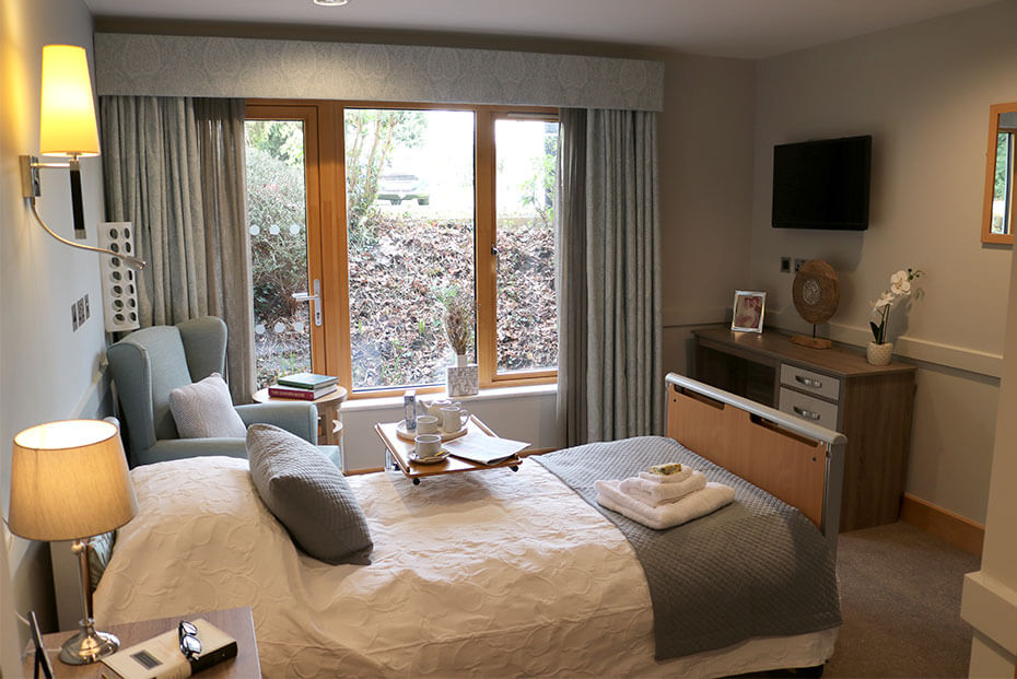 Beautifully laid out bedroom with a large bed, side tables, a chair, a television, and a window showing outdoor greenery