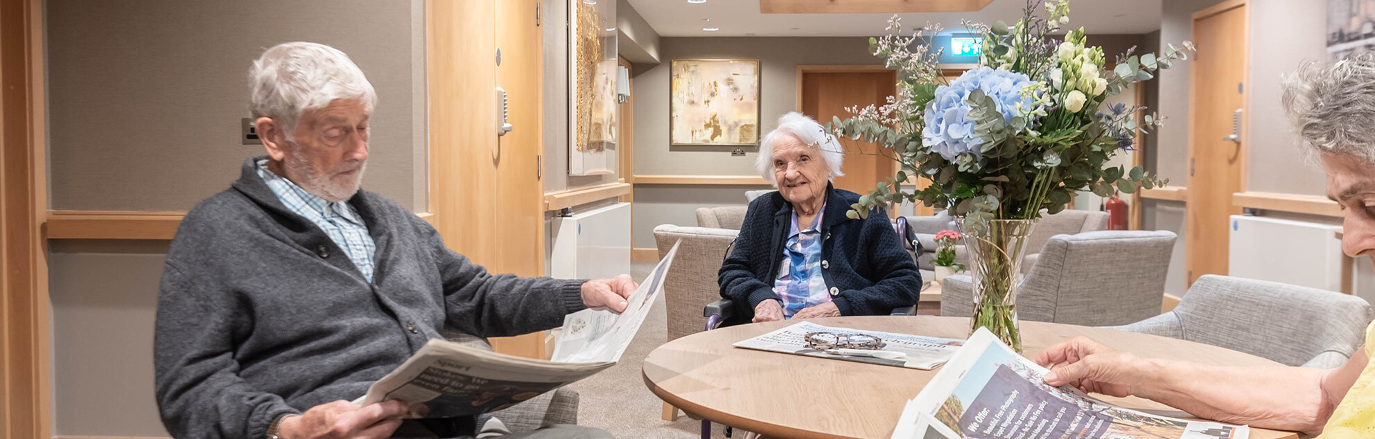 A older man and elderly lady sit together socialising and reading newspapers