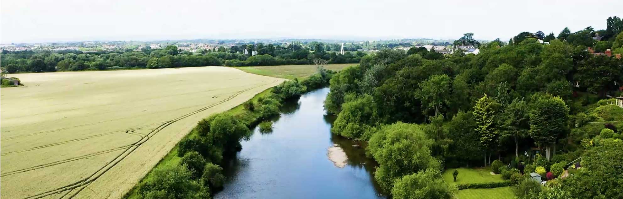 Aerial view of a winding river flowing through fields, with nearby trees and houses