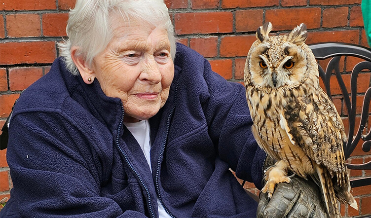 An elderly lady holding an owl on their arm outside