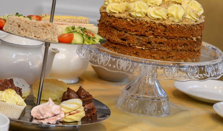 An assortment of cakes and sandwiches on a serving stand, with a multi-layer cake on a glass stand as the centrepiece