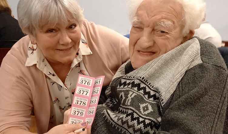 An elderly man and woman at a table, one holding a strip of raffle tickets