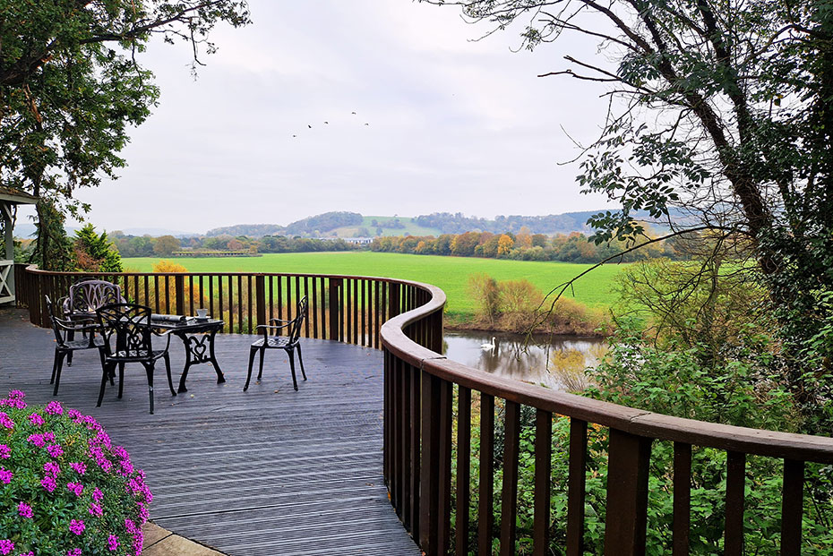 A scenic countryside landscape with a meandering river, lush greenery, and rolling hills under a clear sky