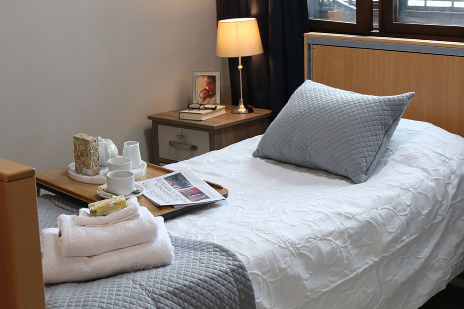 A well-arranged bedroom with a breakfast tray on the bed and a nightstand with a lamp and framed photo beside it