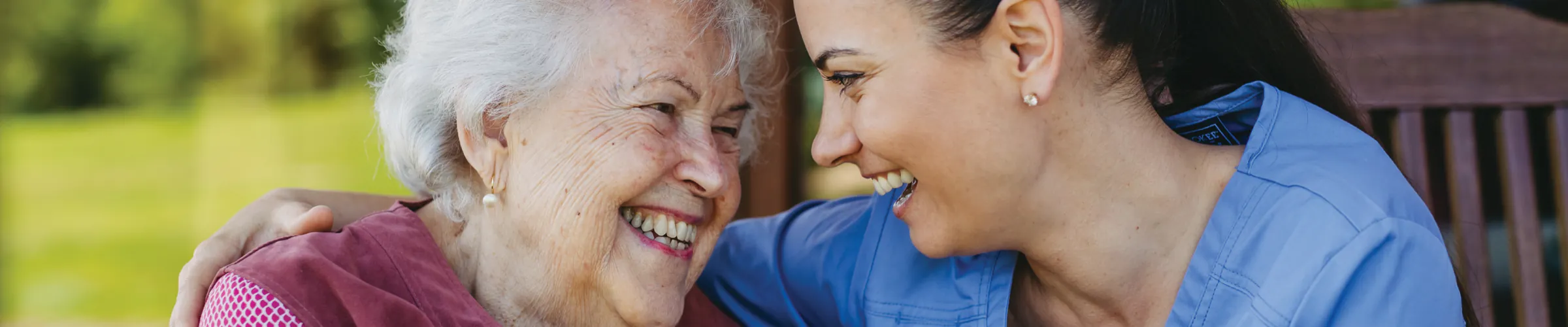 An older woman laughing with a carer who has an arm around her shoulders