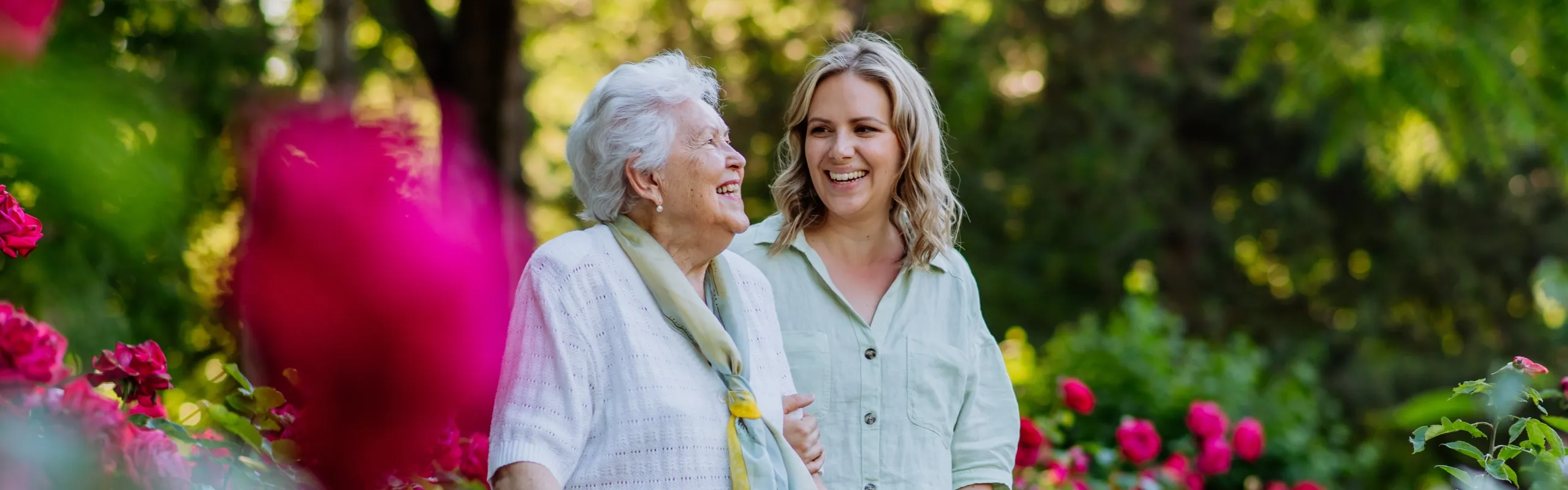 An elderly woman and her daughter smiling together in a rose garden
