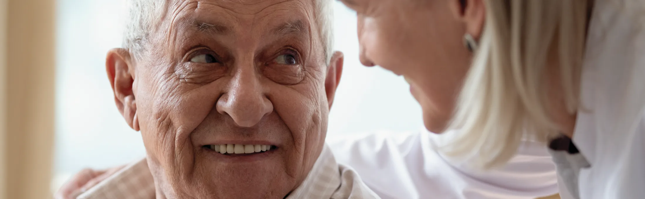 A smiling older man looking round at a carer who has her arm around his shoulders