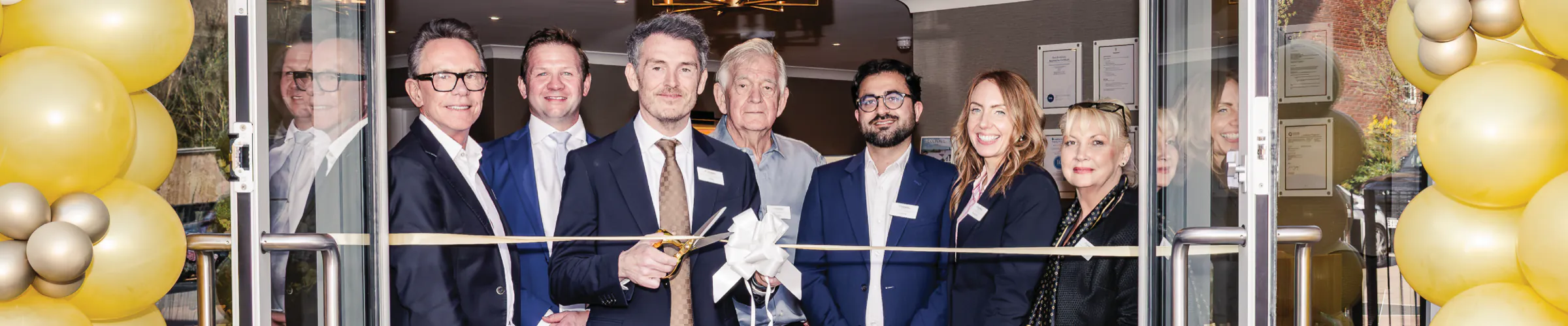 The Rotherwood leadership team cutting a gold ribbon at the opening of Colwall care home, framed by gold balloons