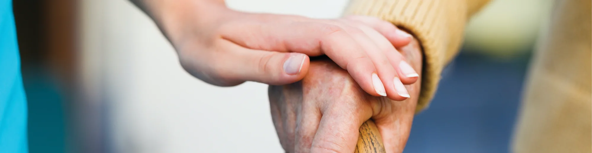 A carer resting a hand on the hand of an older person holding a wooden walking stick