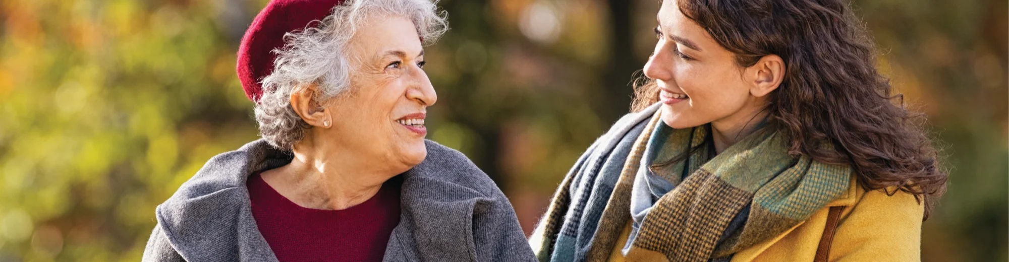 An older woman in a red beret and her daughter smiling at each other on an autumn walk