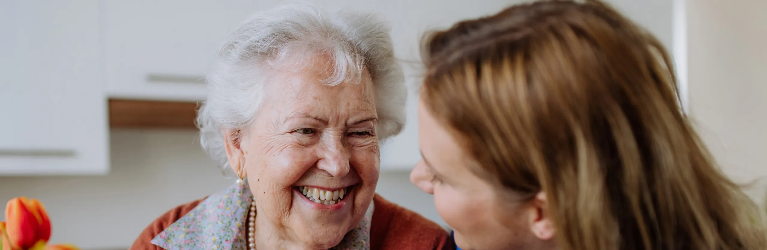 An elderly woman laughing with a carer beside her in a kitchen