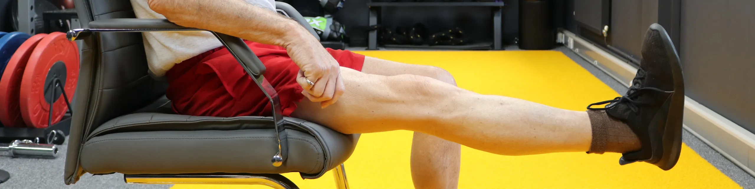 An older person seated in a gym chair extending one leg during a seated exercise