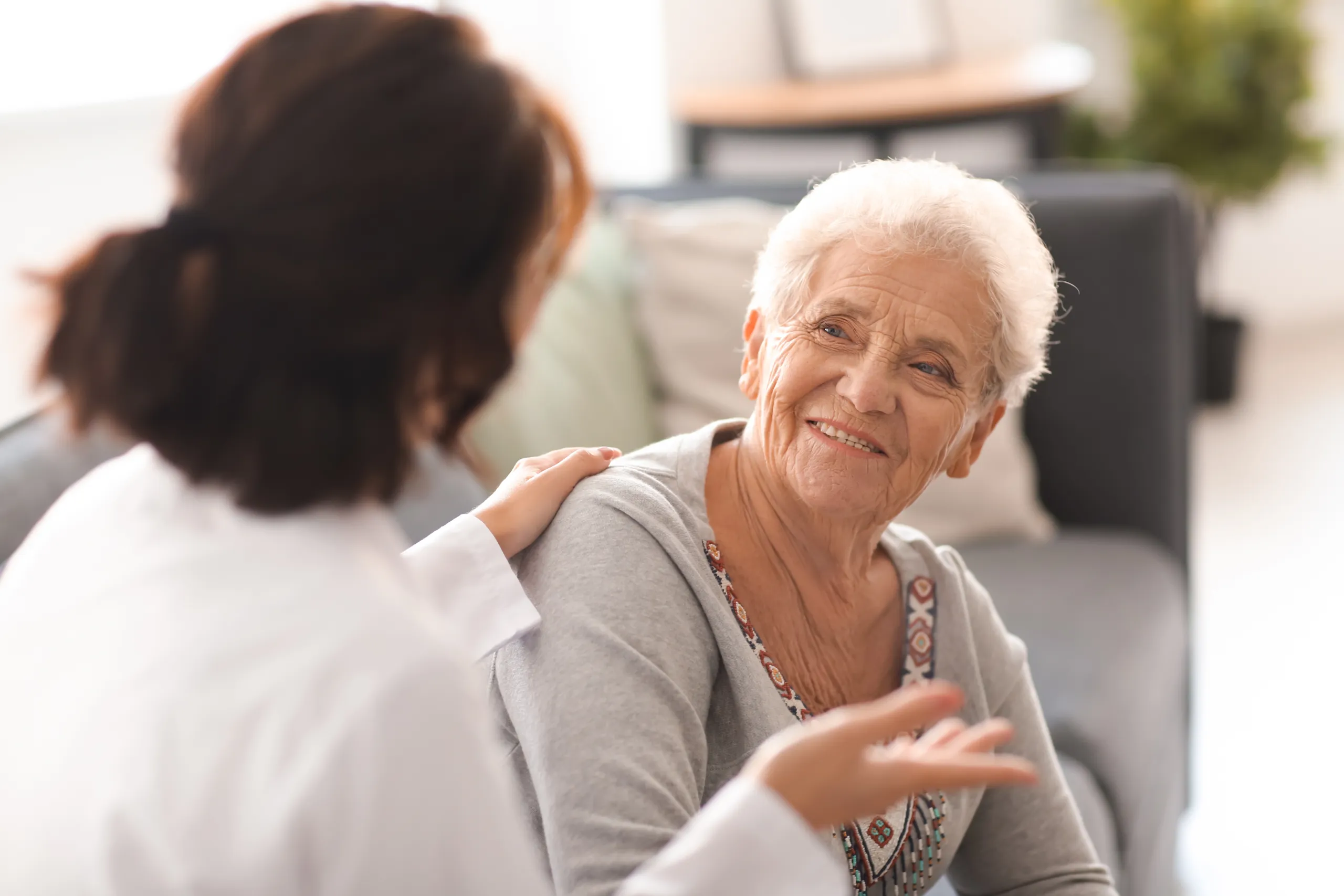 A carer resting a hand on the shoulder of a smiling elderly woman