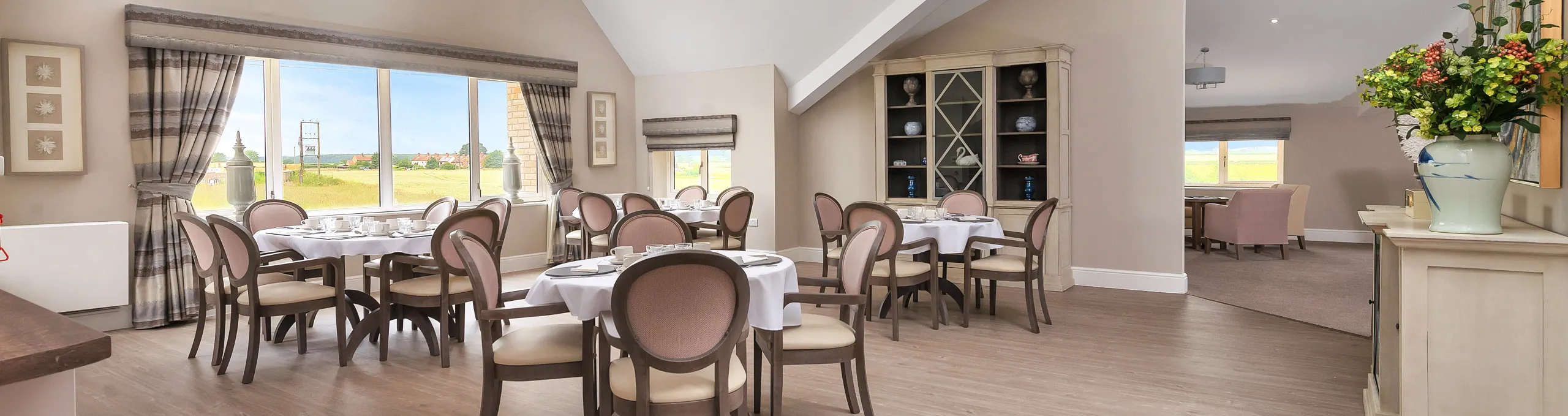 A dining room at Roden Hall with laid tables and countryside views through large windows