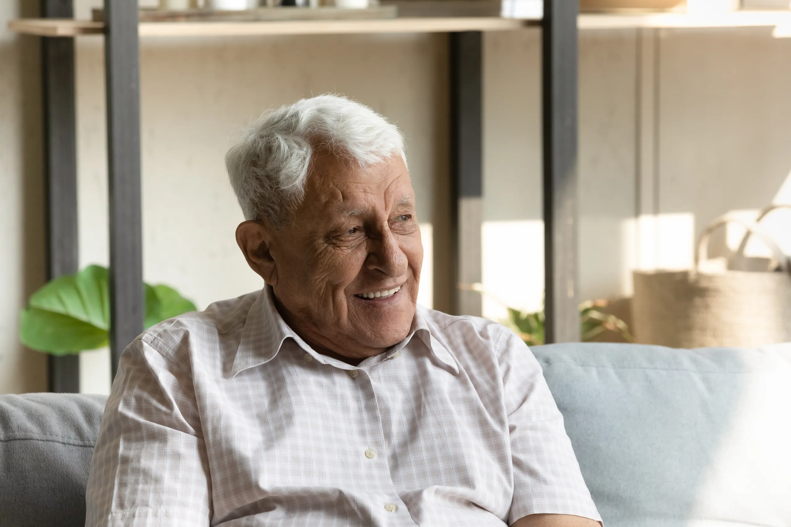 An older man smiling while sitting on a sofa in a bright care home lounge
