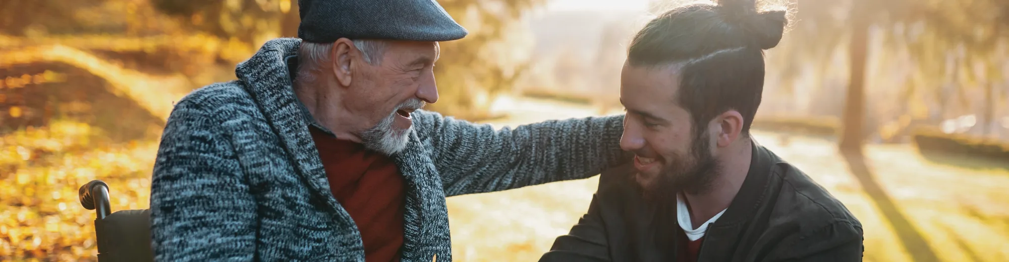 An older man in a flat cap laughing with his son on an autumn walk through the park