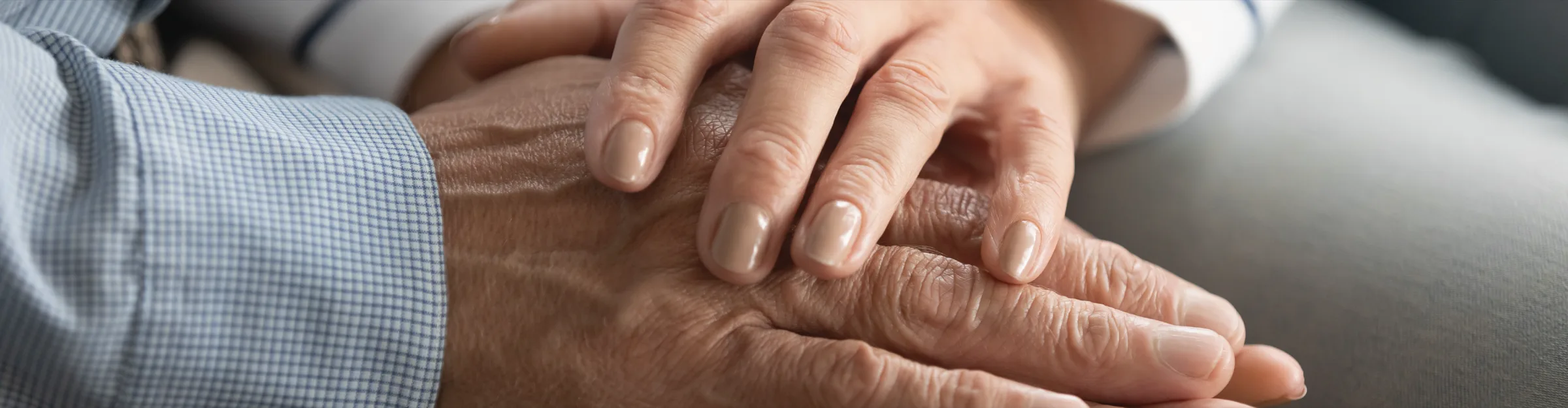 A younger person’s hand resting reassuringly on the hand of an older man