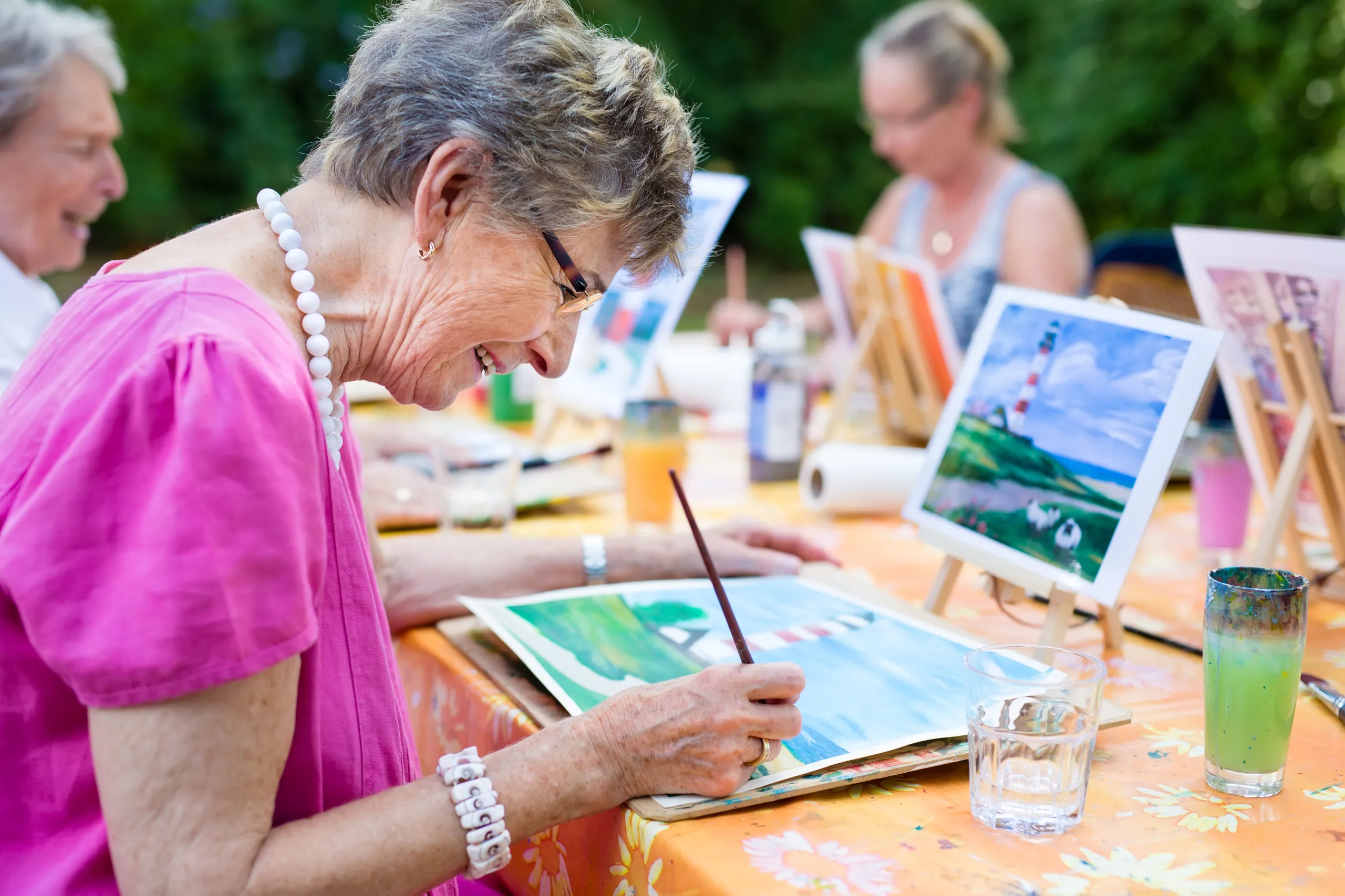 An elderly woman painting a watercolour at an outdoor art session