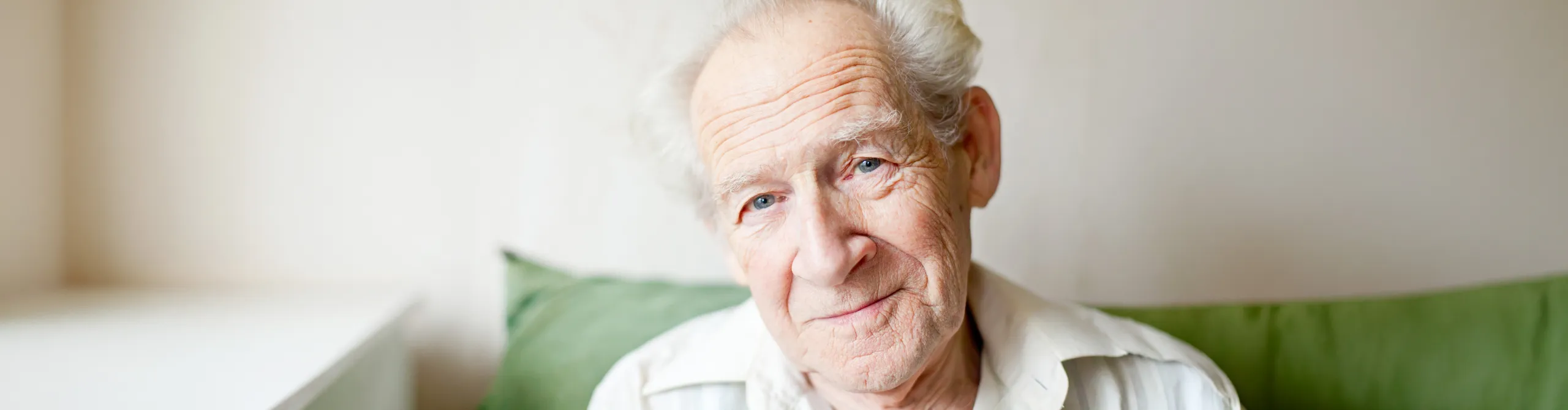 An elderly man smiling while sitting on a sofa with green cushions