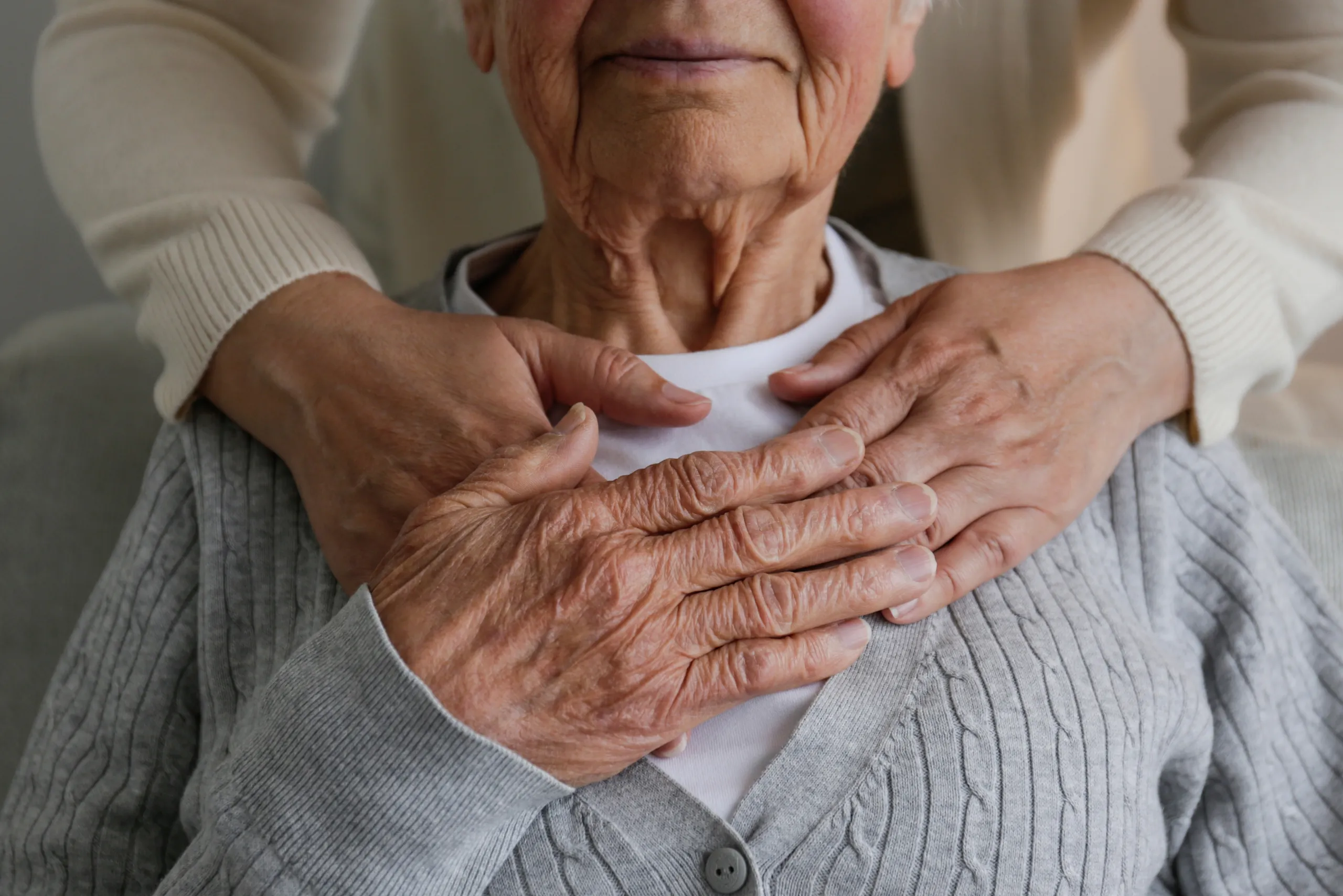 A carer’s hands gently clasped over those of a seated older resident