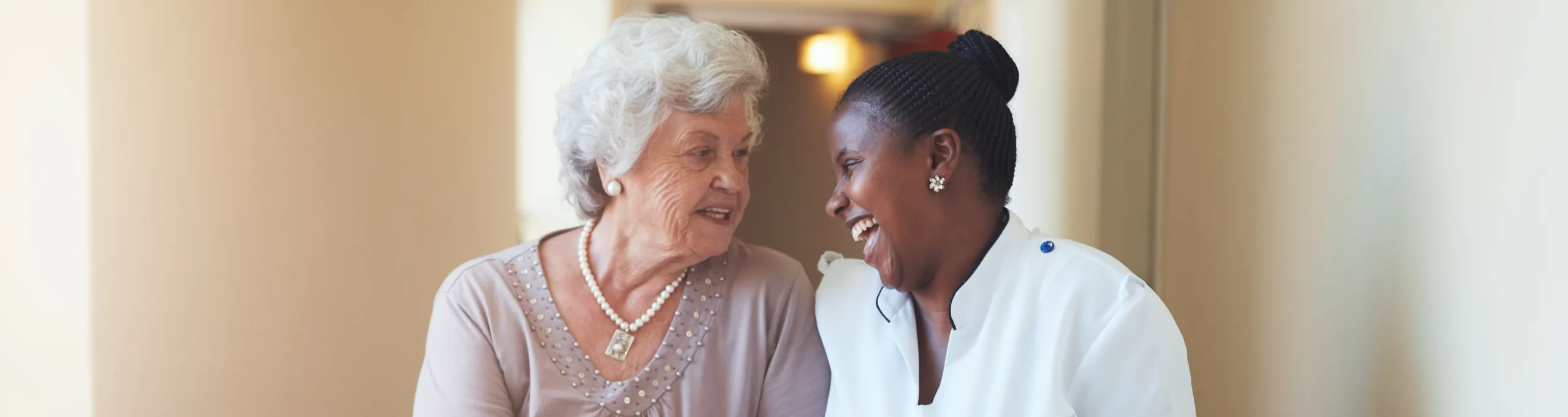 An elderly woman and a carer laughing together in a corridor