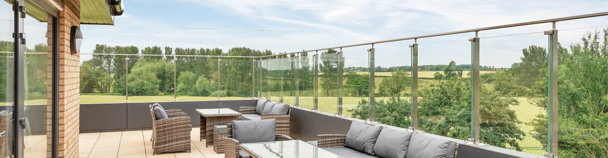 A glass-balustraded care home terrace with rattan seating overlooking open countryside