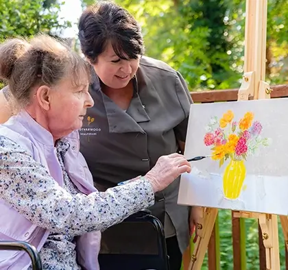 A lifestyle coordinator supports a an older lady to do art outside