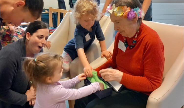 A group of nursery children interacting with an older lady who is seated