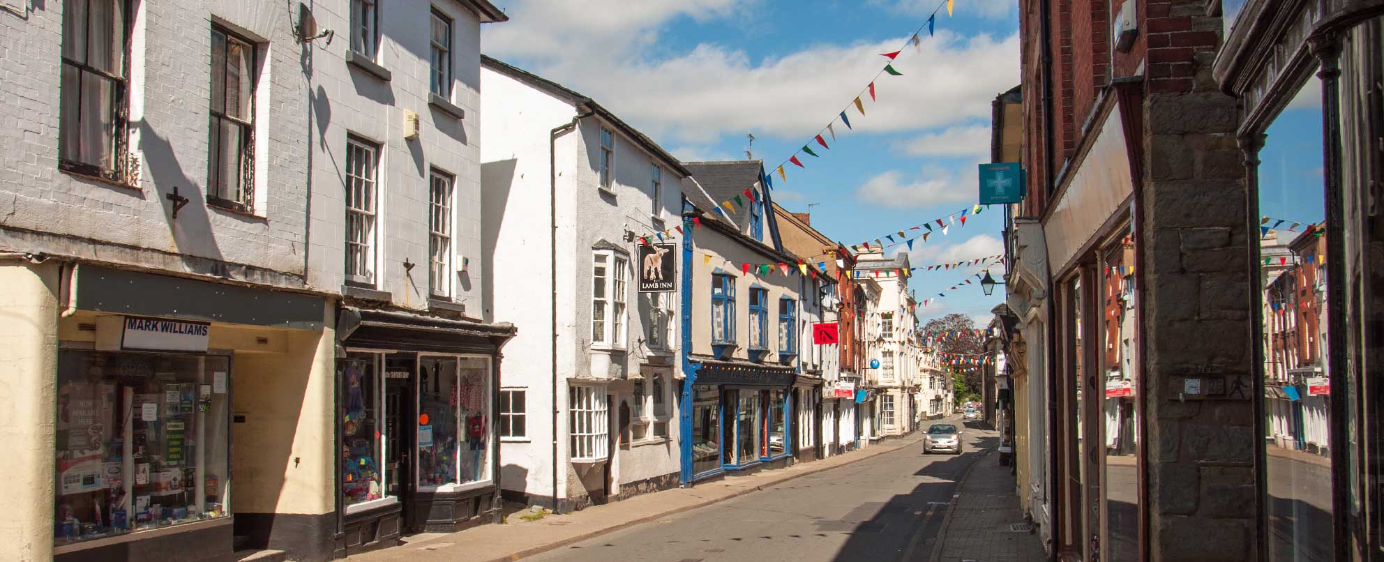 A quaint highstreet with historic buildings, shops and colourful bunting flags on a sunny day