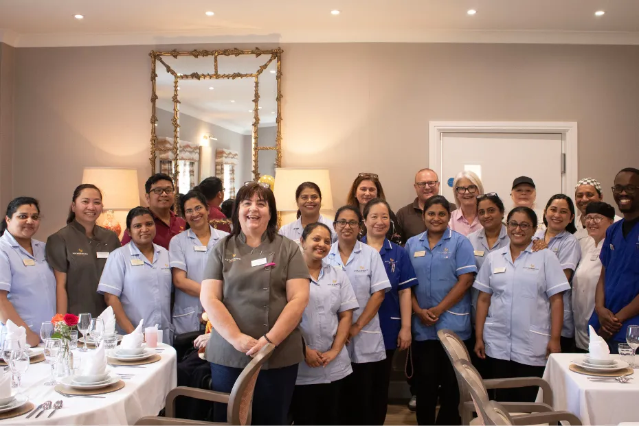 The Kington Court care team smiling together in the dining room, with carers and nurses in blue and grey uniforms