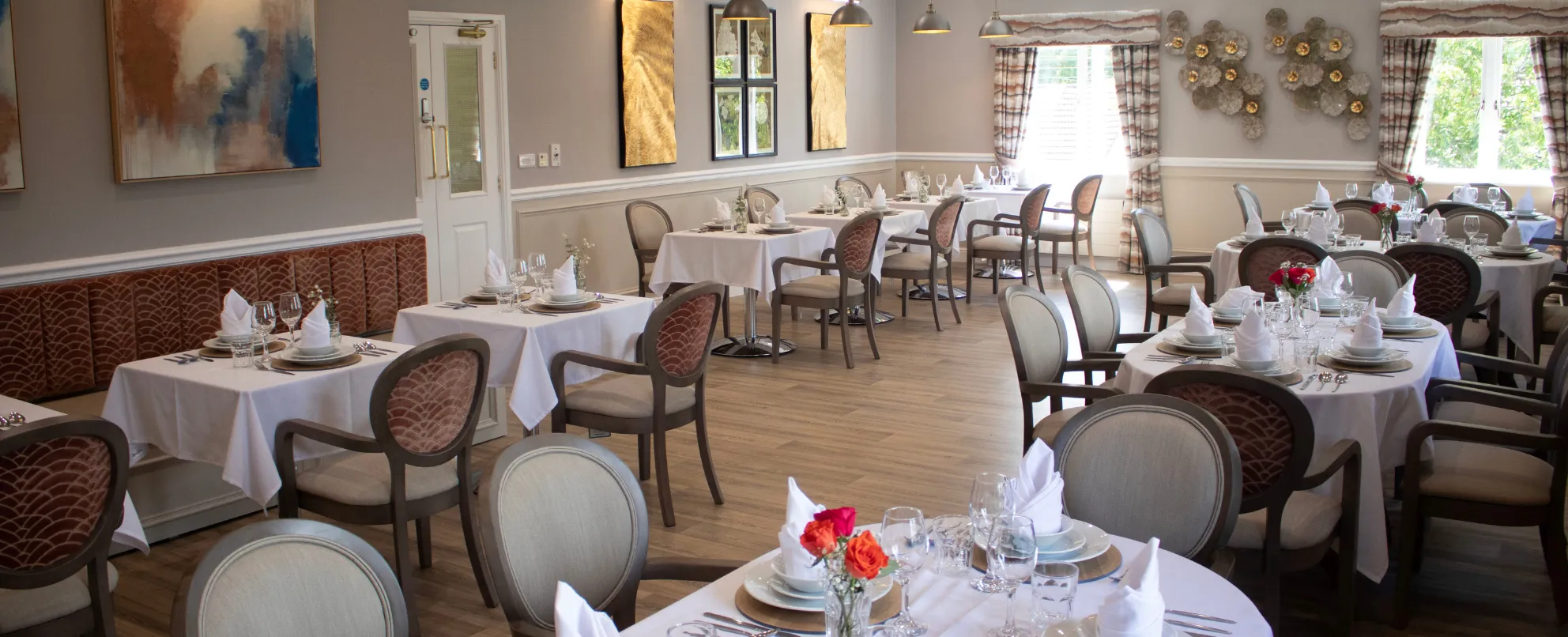 Elegant dining room with white-clothed tables, upholstered chairs and floral centrepieces