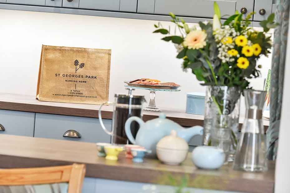 Kitchen countertops with a bouquet of flowers, and various kitchen items. A bag with the text ‘St George's Park’ is visible in the background